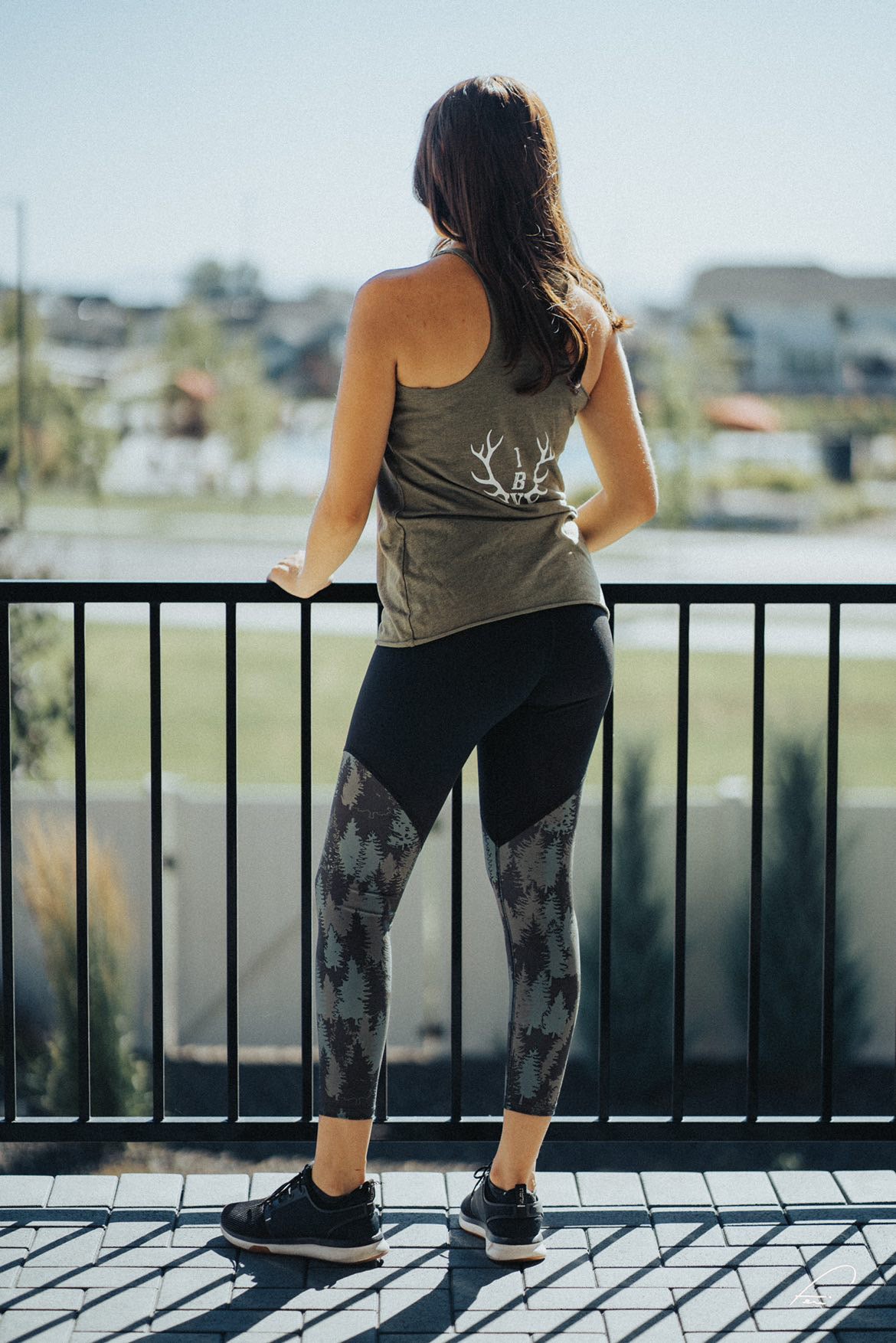 Made in USA 7/8 Green and Black Aspen Leggings. Model by woman outside standing on deck overlooking community. 